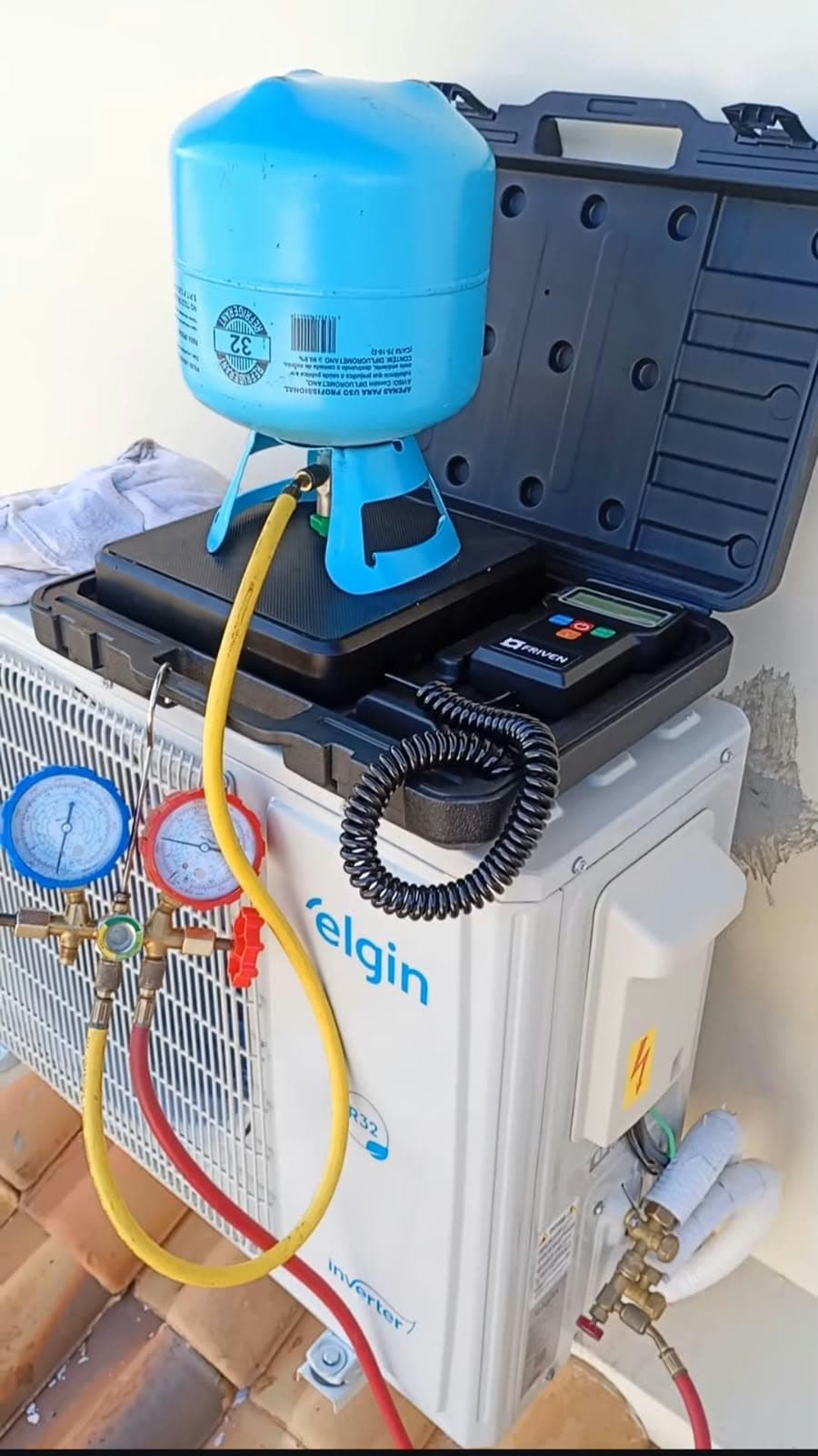 Cilindro de gás R32 sobre a balança de carga, com o manifold ligado à condensadora